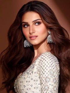 an image of a woman with long brown hair wearing earrings and a white dress in front of