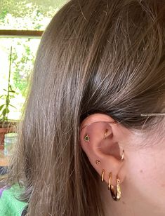 a close up of a person's ear wearing gold hoops and piercings