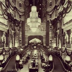 an ornately decorated lobby with chandeliers and tables on the second floor is seen in this black and white photo