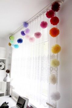 a laptop computer sitting on top of a desk under a window covered in pom - poms