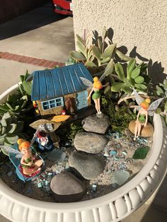 a potted planter filled with small fairy figurines and rocks in front of a house