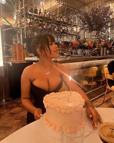 a woman sitting at a table in front of a cake with a lit candle on it