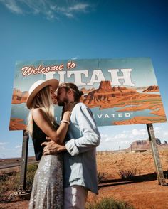 a man and woman kissing in front of a welcome to utah sign