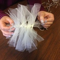 two hands are holding something white on a wooden table with string lights attached to it