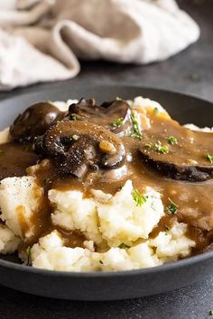 mashed potatoes with mushrooms and gravy in a black bowl on a table