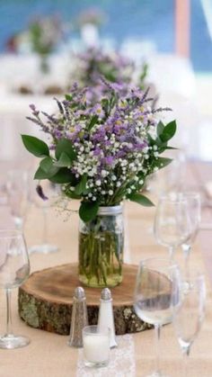 there is a vase with flowers in it on top of a wooden table surrounded by wine glasses