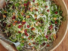 a wooden bowl filled with salad topped with shaved cranberries and almonds next to a fork