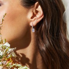 a close up of a woman wearing earrings with flowers in front of her face and behind her ear