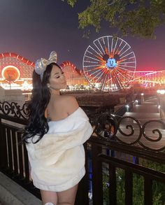 a woman in a white dress standing next to a fence with ferris wheel in the background