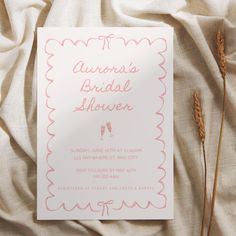 a pink and white bridal shower card on top of a bed next to dried flowers