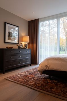 a bedroom with a bed, dresser and large glass doors that look out onto the woods