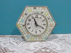 a small clock sitting on top of a lace covered tablecloth next to a blue wall