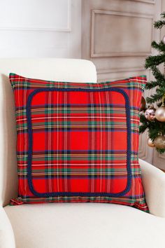 a red plaid pillow sitting on top of a white chair next to a christmas tree