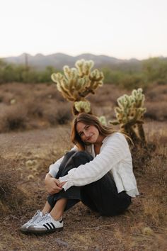 a woman sitting on the ground next to a cactus