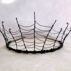 a black wire basket with spider webs on the top and bottom, sitting on a white surface