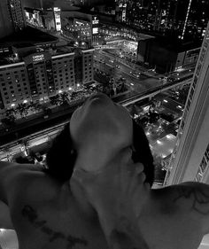 a man with no shirt on standing in front of a window looking at the city