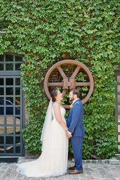 a bride and groom standing in front of a wall covered with green ivys at their wedding