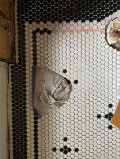 an overhead view of a bathroom with black and white tiles on the floor, toilet paper in the middle