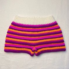 a close up of a knitted shorts on a white surface with a pink and orange stripe