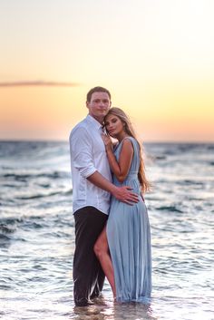 a man and woman standing in the ocean at sunset with their arms around each other