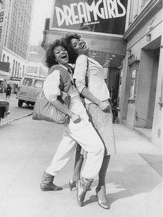 two people standing on the sidewalk in front of a movie theater with their mouths open