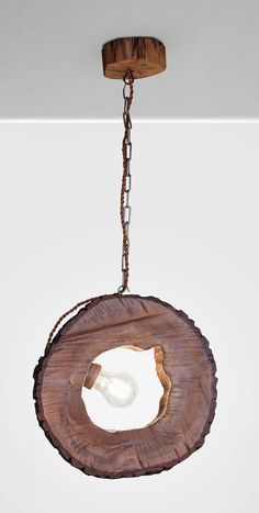 a wooden light fixture hanging from a chain on a white wall behind it is a piece of wood that has been cut in half