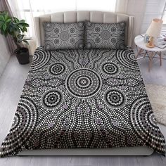 a bed covered in a black and white bedspread next to a window with potted plants