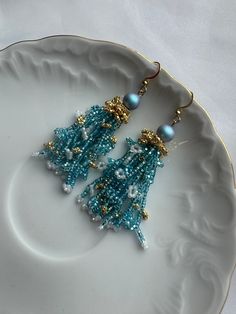 Discover the beauty of these handcrafted blue and gold seed bead earrings, accentuated with a sparkling zircon stone. Expertly made with attention to detail, these earrings offer a blend of elegance and charm, ideal for any occasion. The intricate design showcases vibrant colors that enhance their appeal, ensuring they complement both casual and formal attire with grace. Each pair is crafted uniquely, guaranteeing both quality and individuality. Treat yourself or a loved one to these exquisite earrings, perfect for adding a touch of sophistication to any outfit. Comes in a Cardboard box, ready to be a perfect gift for you or someone you want to make happy. P.S.   box, not the same as on the picture. Bohemian Blue Earrings With Gold Beads, Blue Gold Beaded Drop Earrings, Light Blue Beaded Dangle Earrings For Party, Blue Dangling Beads Earrings For Festive Occasions, Blue Dangle Earrings With Gold Beads, Elegant Turquoise Beaded Earrings With Gold Beads, Blue Crystal Earrings With Dangling Beads For Gift, Elegant Turquoise Earrings With Gold Beads, Festive Blue Earrings With Dangling Beads