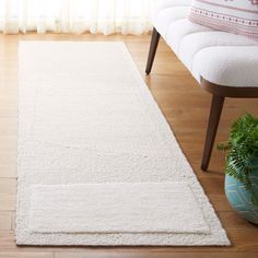 a white rug is on the floor in front of a chair and potted plant