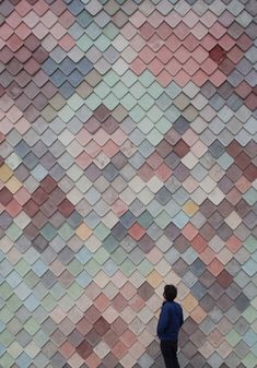 a person standing in front of a wall made out of small colored tiles, looking up at the sky