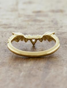 a gold wedding band with leaves on the side and an arrow in the middle, sitting on a wooden surface