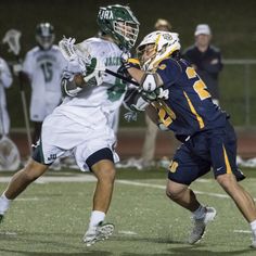 two men playing lacrosse on a field with people watching