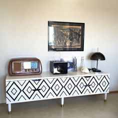 a white and black dresser with a clock on top next to a painting hanging on the wall