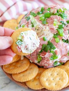 a person is holding a cracker over a cheese ball with ham and celery on it