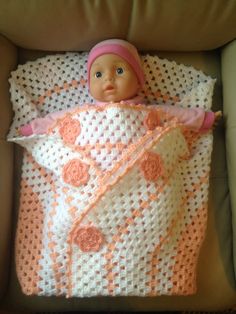 a baby doll laying in a crocheted blanket on top of a couch next to a pillow