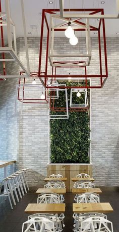 an indoor dining area with tables and chairs, plants on the wall behind them in red frames