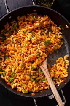 a skillet filled with macaroni and cheese being stirred by a wooden spoon