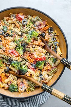 a skillet filled with pasta salad and two wooden spoons sitting on the side