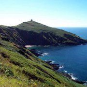 a grassy hill next to the ocean with an island in the middle and water on top