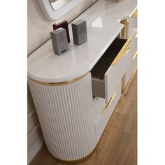 a white vanity with gold trim around the drawers and mirror on the wall behind it