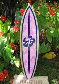 a pink surfboard sitting on top of a wooden stand in front of some flowers