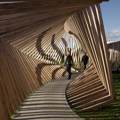 two people walking down a wooden walkway in front of an art installation on the grass