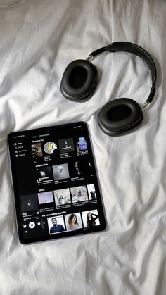 a tablet with headphones on it sitting on a white sheeted bed next to an mp3 player