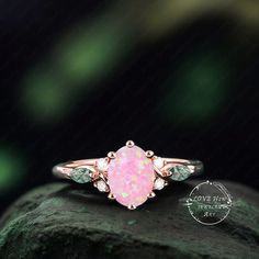 a pink opalite and diamond ring sitting on top of a rock