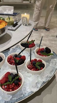 four bowls filled with fruit on top of a glass table next to a plate of food