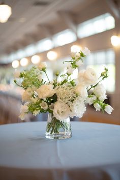 a vase filled with white flowers sitting on top of a blue tablecloth covered table