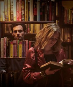 a man and woman standing in front of a bookshelf with many books on it