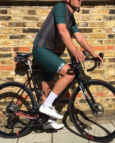 a man is riding his bike in front of a brick wall and wearing green shorts