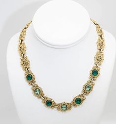 "This unusual necklace, of which the back of each medallion is scored and detailed, is 17 ½\" and ½\" wide. The center medallion holds dark green and aqua stones highlighting the detailed design." Traditional Luxury Emerald Necklace With Intricate Design, Luxury Ornate Green Necklace, Luxury Green Bohemian Necklace, Luxury Green Art Deco Necklace, Vintage Green Statement Necklace, Cheap Green Vintage Necklace, Luxury Green Collectible Necklace, Luxury Collectible Green Necklace, Aqua Stone