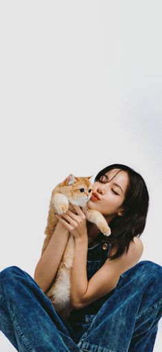 a woman sitting on the ground holding a cat up to her face with both hands